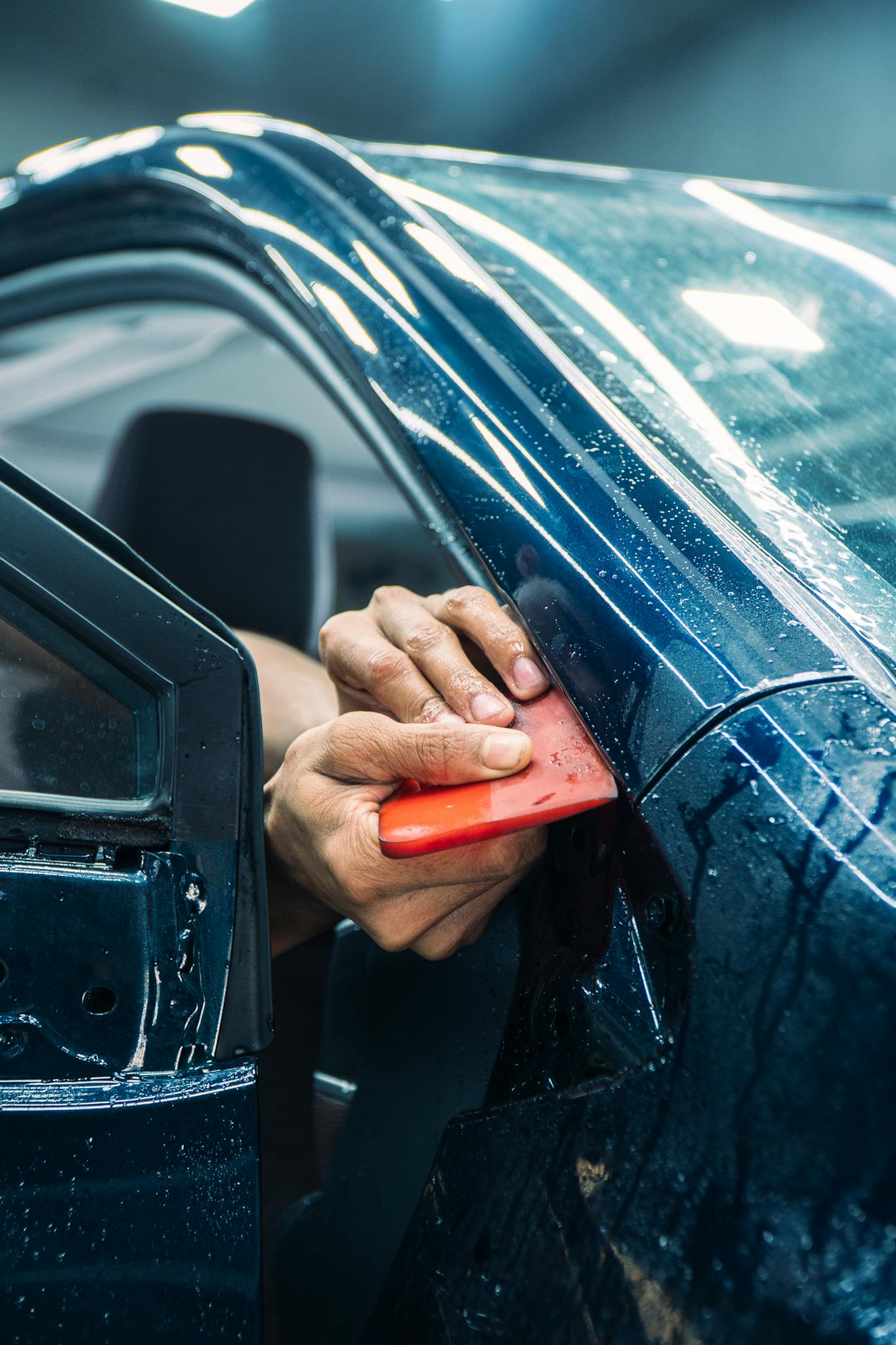 Close-up of a technician installing PPF on a car door in a workshop.