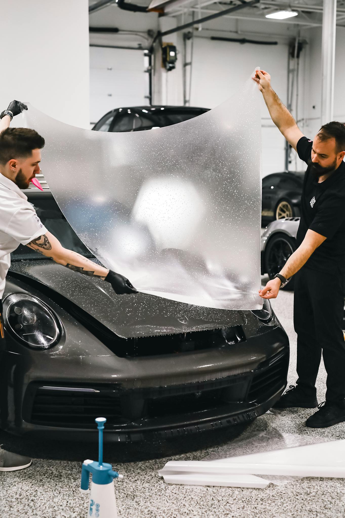 Two technicians applying a protective film on a sleek sports car in a garage setting.